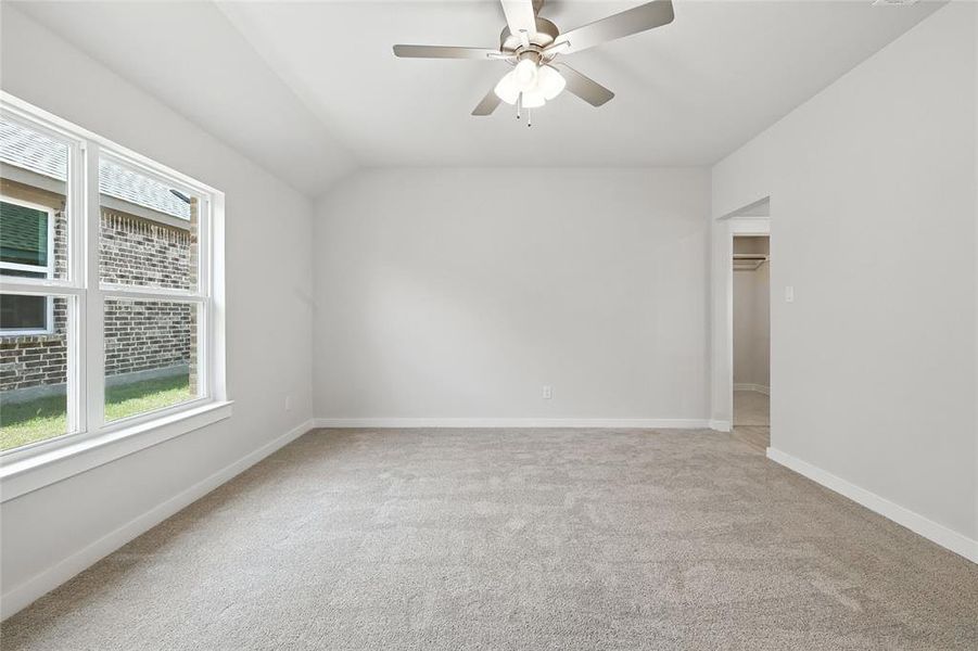 Carpeted empty room with plenty of natural light, vaulted ceiling, and ceiling fan