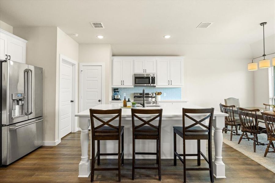 Kitchen featuring appliances with stainless steel finishes, decorative backsplash, white cabinets, a center island with sink, and a breakfast bar