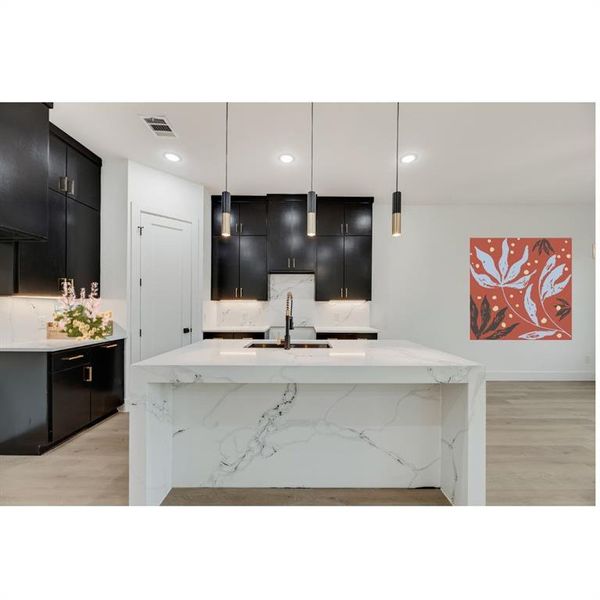 Kitchen featuring light granite countertops, dark cabinetry, decorative light fixtures, light wood-style floors, and recessed lighting