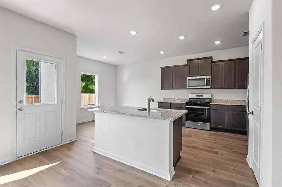 Kitchen featuring appliances with stainless steel finishes, recessed lighting, light stone counters, dark brown cabinetry, and an island with sink