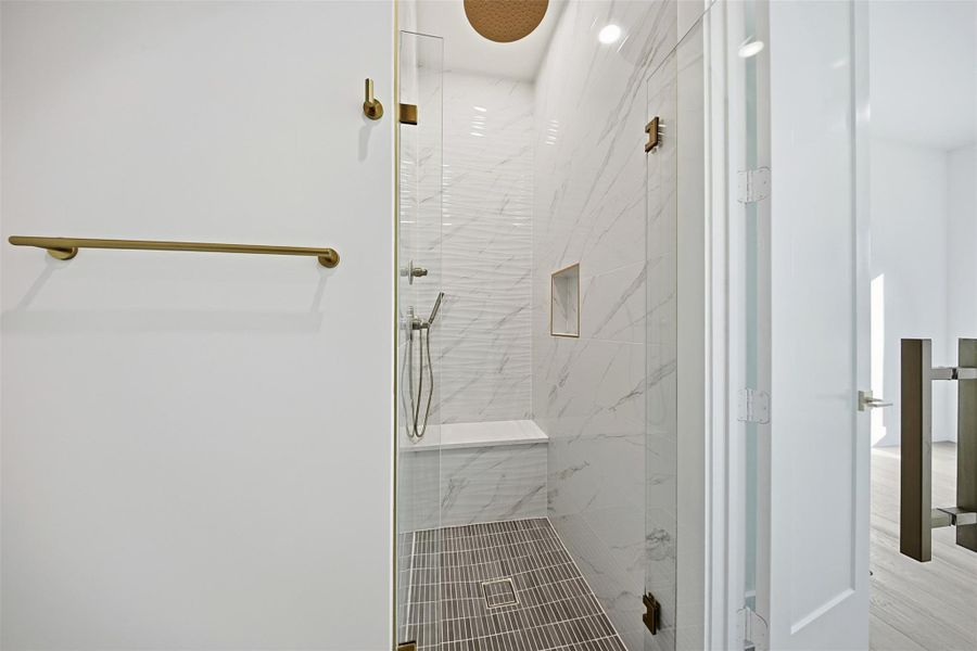 Same floorplan - different finishes. The walk-in shower is designed with marble-patterned wall tiles, a built-in bench, and high-end gold-toned fixtures.