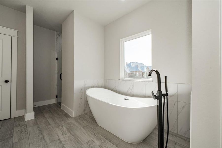 Primary bathroom featuring a freestanding tub, tile walls, wood finished floors, and a wainscoted wall Primary bathroom featuring a freestanding tub, tile walls, wood finished floors, and a wainscoted wall