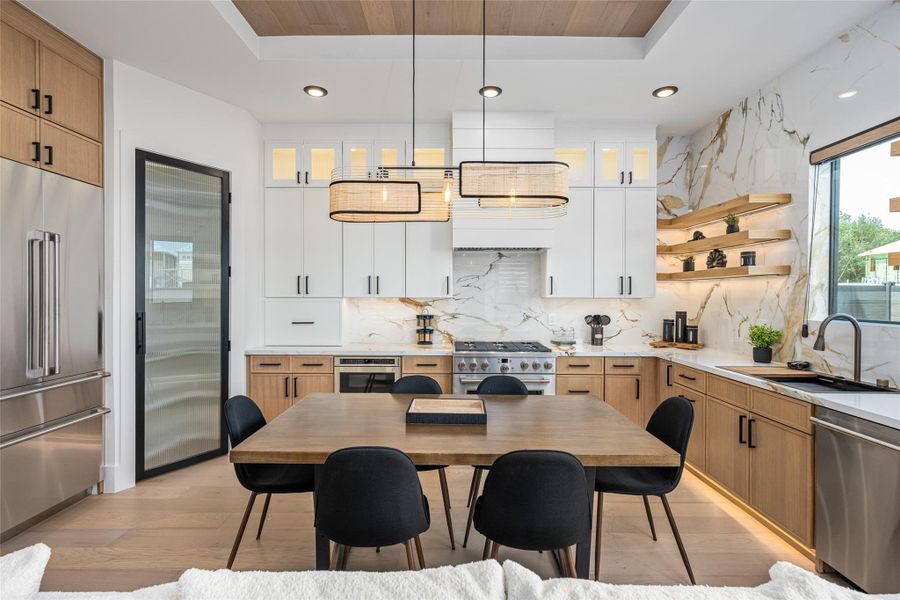 The gourmet kitchen is a true showpiece with two-tone custom cabinetry, under-shelf and under-cabinet lighting, GE Café appliances, and a sculptural chandelier beneath vaulted ceilings with wood inlays