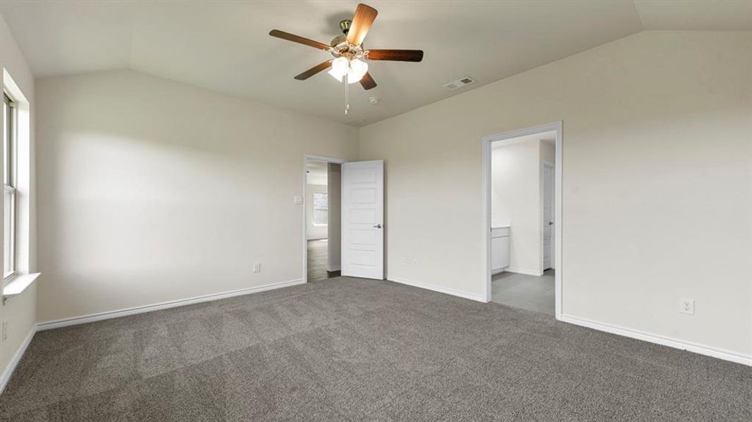 This spacious room features neutral-toned carpet, a vaulted ceiling, and a ceiling fan with light fixture