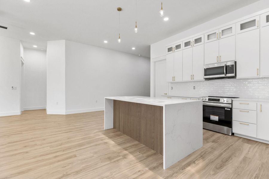 Kitchen with stainless steel appliances, glass fronted cabinets, white cabinetry, light wood-style flooring, and decorative light fixtures
