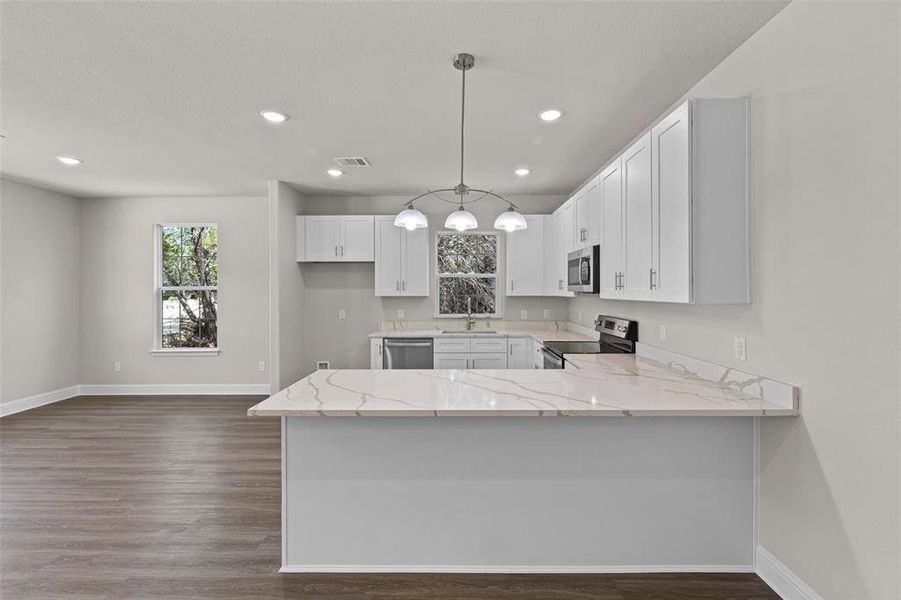 Kitchen with pendant lighting, white cabinetry, kitchen peninsula, stainless steel appliances, and light stone countertops