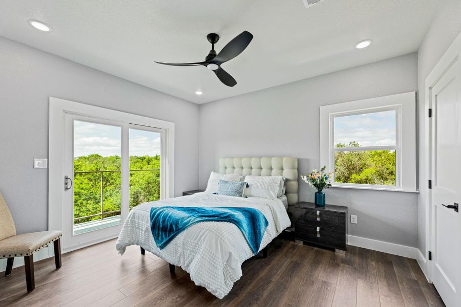 Spacious bedroom featuring wood-finish flooring, a contemporary ceiling fan, recessed lighting, a sliding glass door to an exterior balcony, and an additional large window