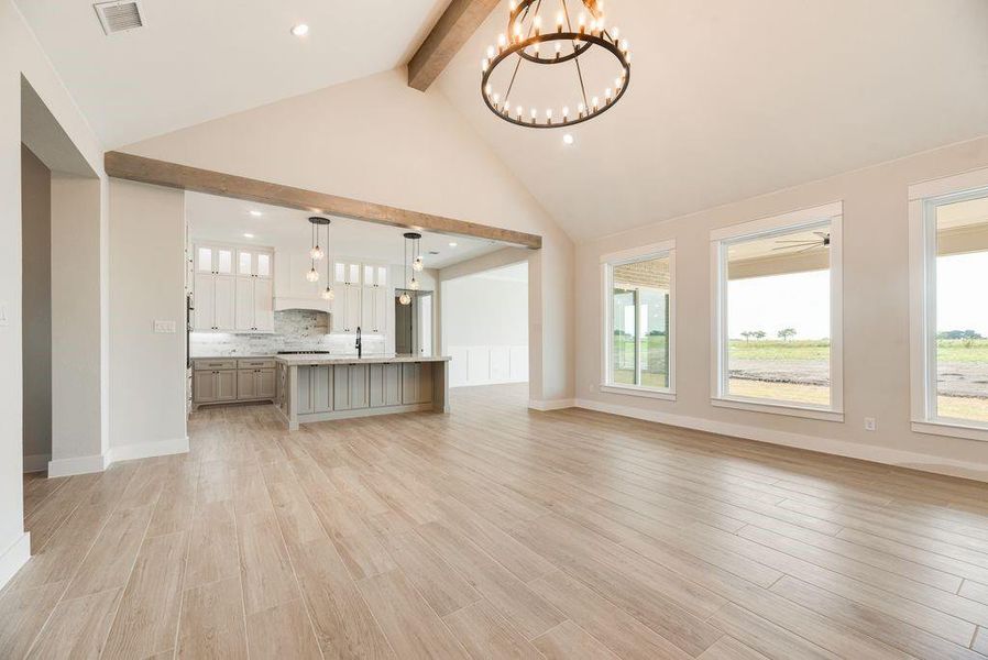 Unfurnished living room featuring beam ceiling, a chandelier, light wood finished floors, high vaulted ceiling, and recessed lighting Unfurnished living room featuring beam ceiling, a chandelier, light wood finished floors, high vaulted ceiling, and recessed lighting