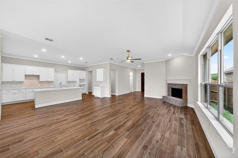 Open-concept living area featuring wood-finish flooring, a brick fireplace with a mantle, and large windows
