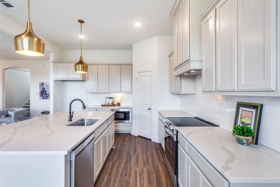 Kitchen with appliances with stainless steel finishes, light stone counters, sink, and a center island with sink