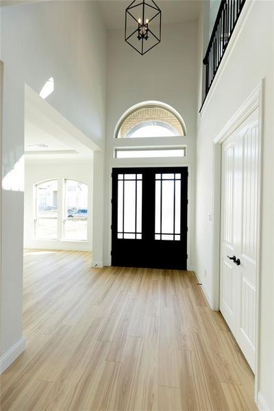 Entryway featuring french doors, a towering ceiling, light hardwood / wood-style flooring, and a notable chandelier