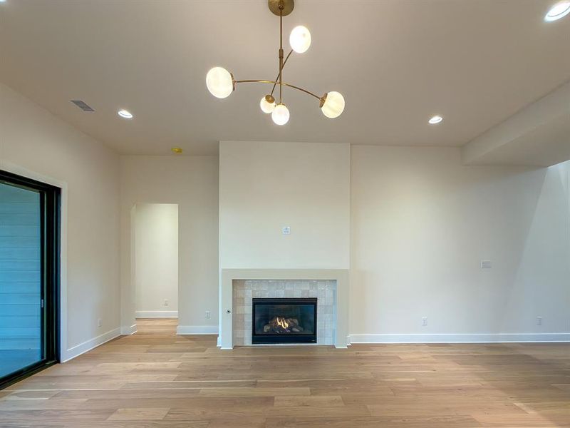 Living area featuring a modern fireplace with a tile surround and mantel, wood-finish flooring, a contemporary chandelier, recessed lighting, and a sliding glass door