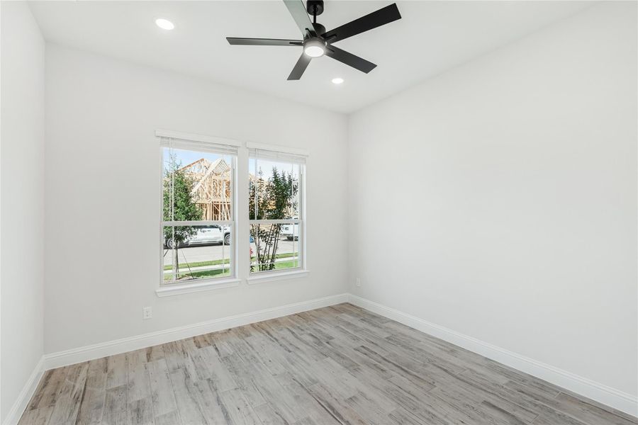 Empty bedroom with light wood floors, black ceiling fan, and double window with natural light