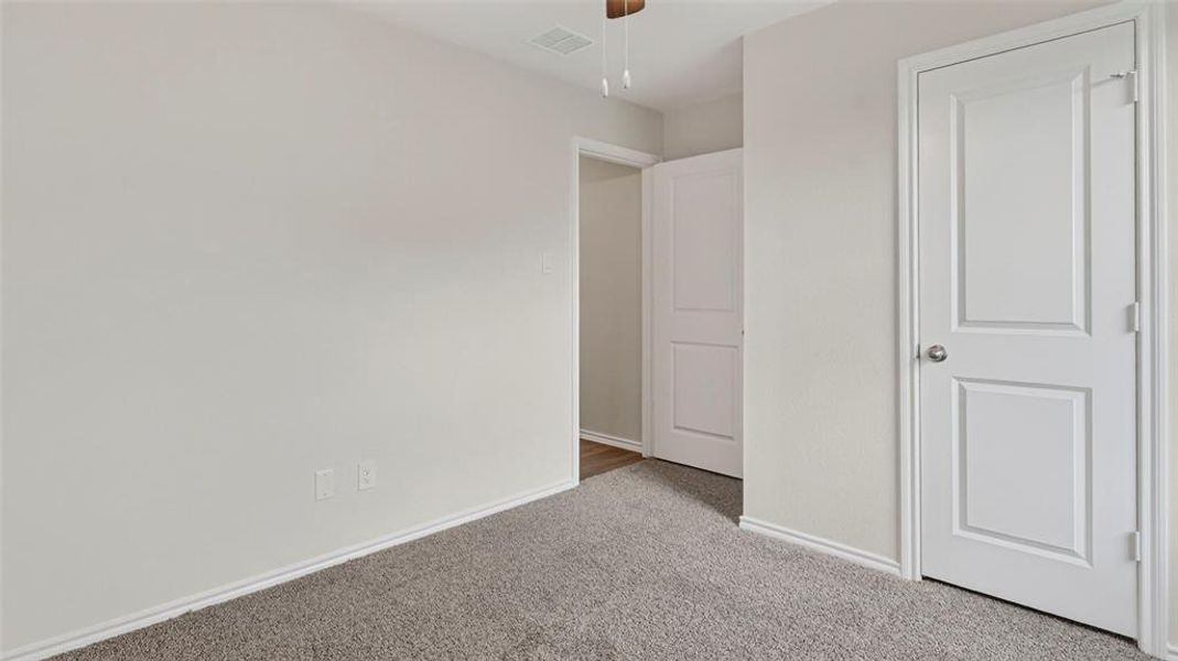 Carpeted room featuring light gray walls, white trim, two paneled interior doors, and a ceiling fan Carpeted room featuring light gray walls, white trim, two paneled interior doors, and a ceiling fan