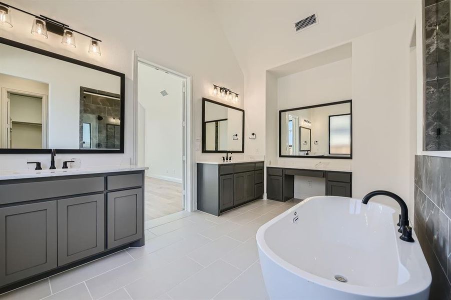 Bathroom with tile patterned flooring, vaulted ceiling, a tub to relax in, and vanity