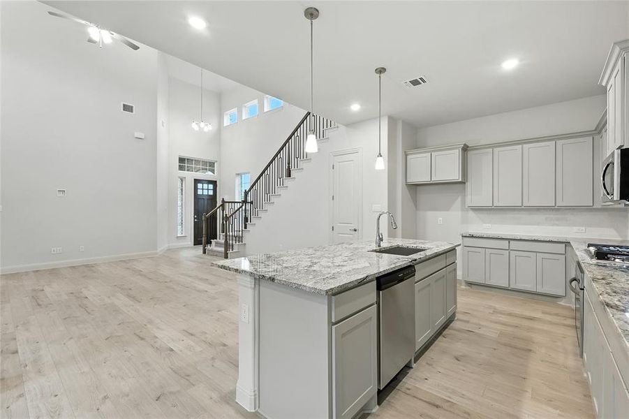Kitchen featuring gray cabinets, light stone counters, recessed lighting, and a towering ceiling