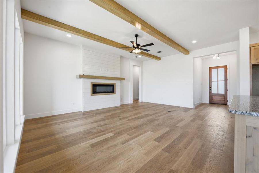 Unfurnished living room featuring light wood finished floors, beam ceiling, a ceiling fan, recessed lighting, and a large fireplace Unfurnished living room featuring light wood finished floors, beam ceiling, a ceiling fan, recessed lighting, and a large fireplace