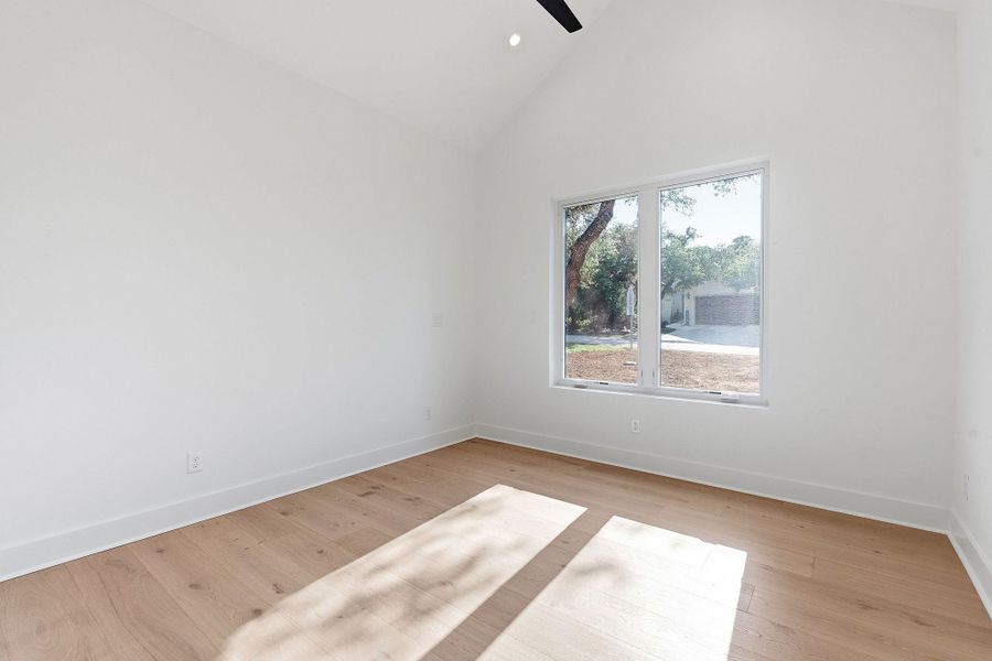 A spacious room features vaulted ceilings, wide-plank wood flooring, and a large window.