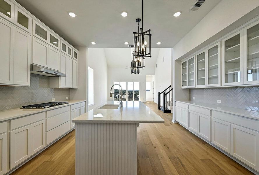 Kitchen with under cabinet range hood, stainless steel gas stovetop, recessed lighting, light countertops, and a chandelier
