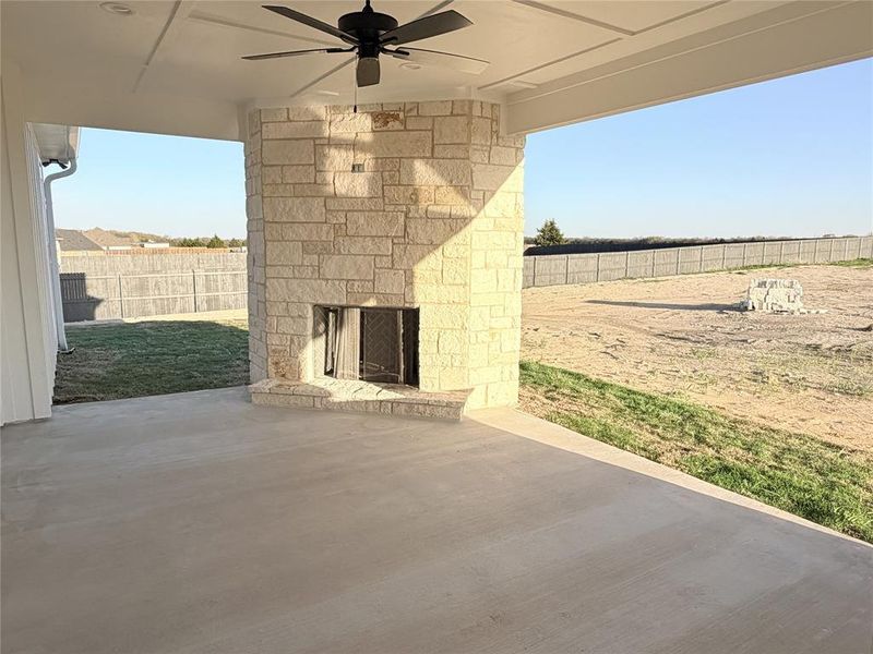 Fenced backyard featuring an outdoor stone fireplace, a patio, and ceiling fan Fenced backyard featuring an outdoor stone fireplace, a patio, and ceiling fan