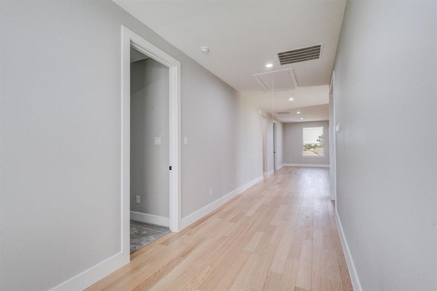 Hallway with light wood-finish flooring, light grey painted walls, white baseboards, and white door casings Hallway with light wood-finish flooring, light grey painted walls, white baseboards, and white door casings