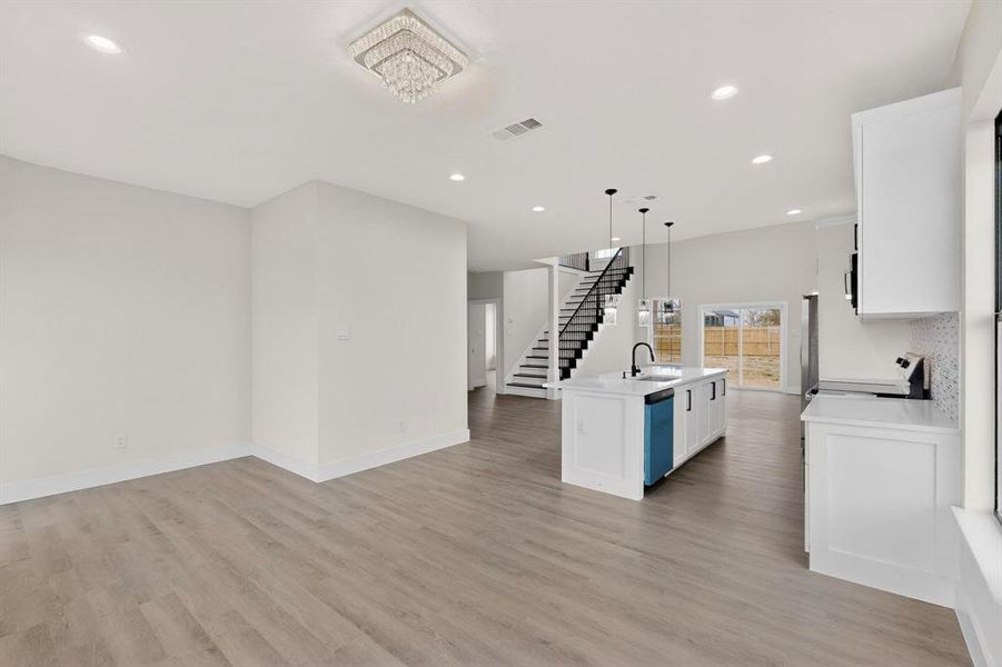 Kitchen with white cabinetry, open floor plan, a center island with sink, pendant lighting, and light wood-style floors Kitchen with white cabinetry, open floor plan, a center island with sink, pendant lighting, and light wood-style floors
