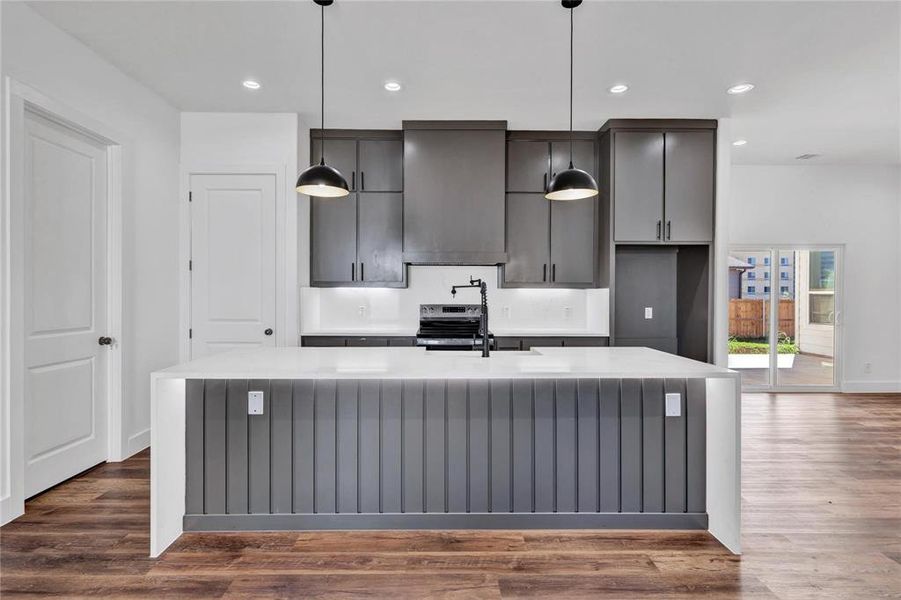 Kitchen with light stone countertops, dark wood-style flooring, stainless steel electric stove, and a large island
