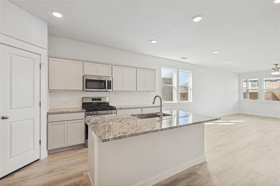 Kitchen featuring light hardwood / wood-style flooring, appliances with stainless steel finishes, a wealth of natural light, and a kitchen island with sink