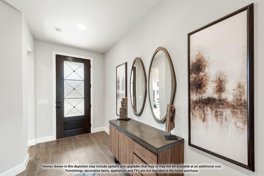 Home entryway with dark wood front door, oval mirrors, wood console table, and hardwood floors