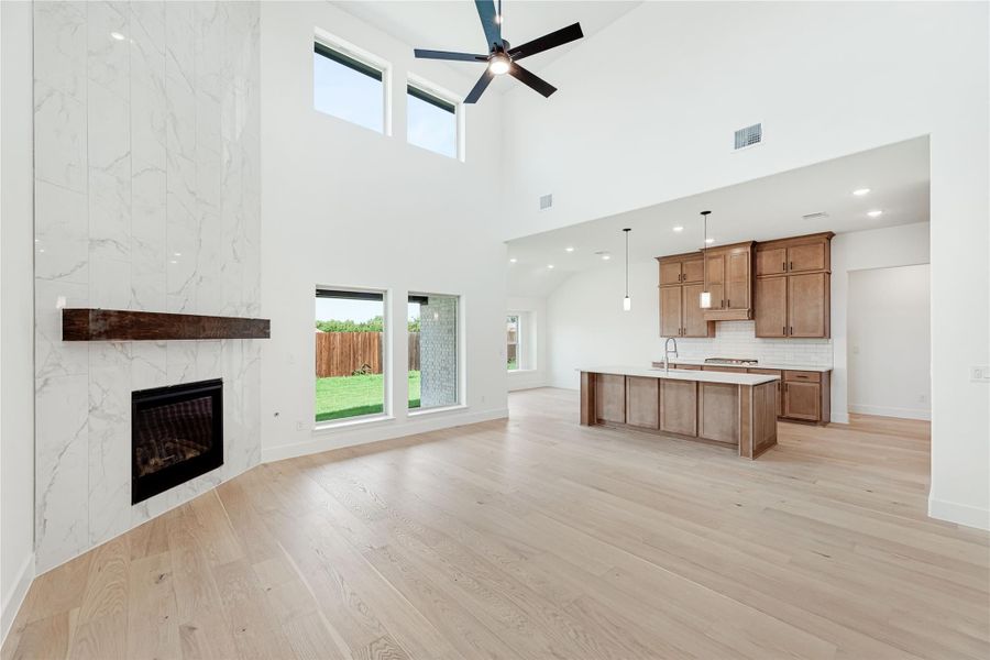 Open living area with marble fireplace, high ceilings, hardwood floors, and open kitchen with island in background Open living area with marble fireplace, high ceilings, hardwood floors, and open kitchen with island in background