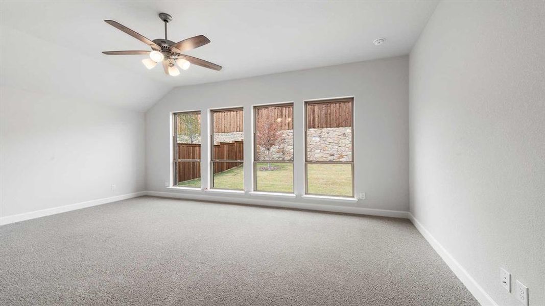 Carpeted spare room featuring vaulted ceiling and ceiling fan