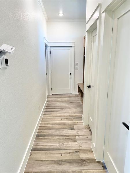 Corridor with light wood finished floors, ornamental molding, and baseboards