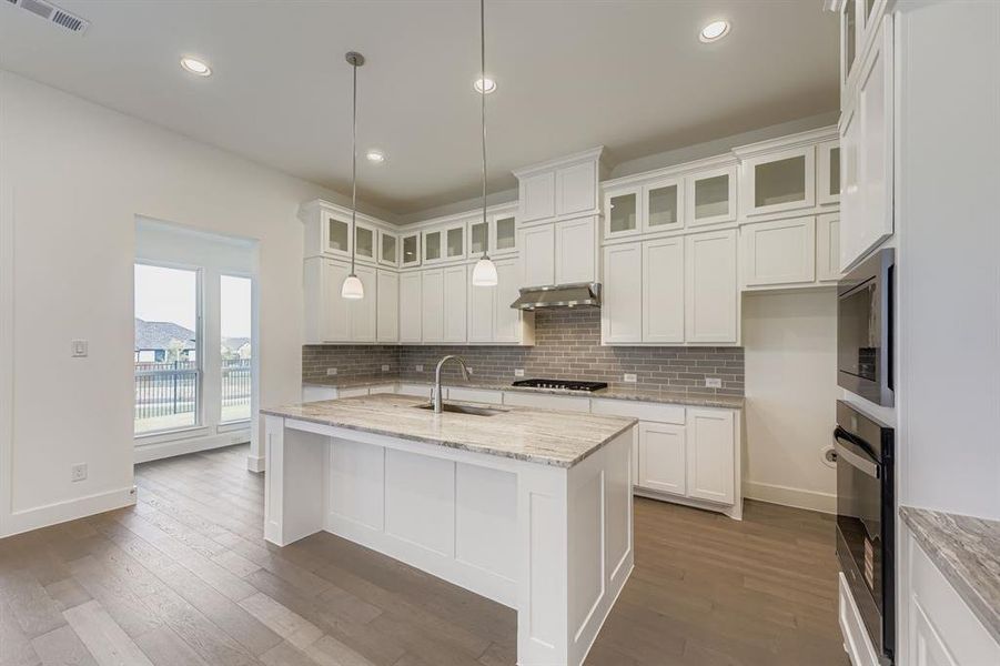 Kitchen featuring decorative backsplash, glass insert cabinets, white cabinetry, light stone countertops, and recessed lighting Kitchen featuring decorative backsplash, glass insert cabinets, white cabinetry, light stone countertops, and recessed lighting