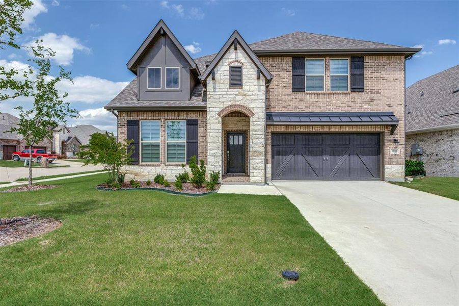 View of front facade with an attached garage, stone siding, concrete driveway, a front lawn, and brick siding