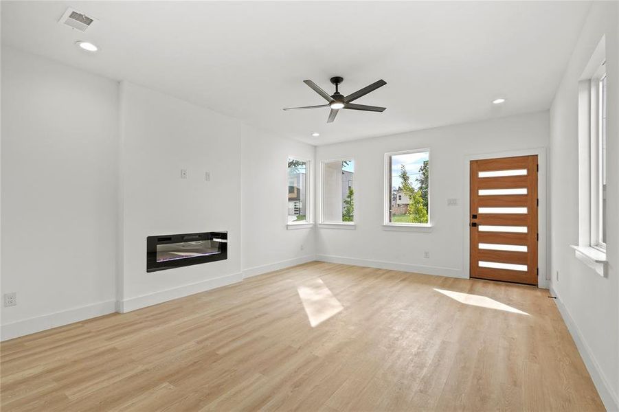 Unfurnished living room with light wood-style flooring, a ceiling fan, recessed lighting, a glass covered fireplace, and baseboards Unfurnished living room with light wood-style flooring, a ceiling fan, recessed lighting, a glass covered fireplace, and baseboards