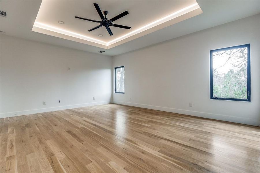 Unfurnished room featuring a tray ceiling, ceiling fan, and light wood-type flooring