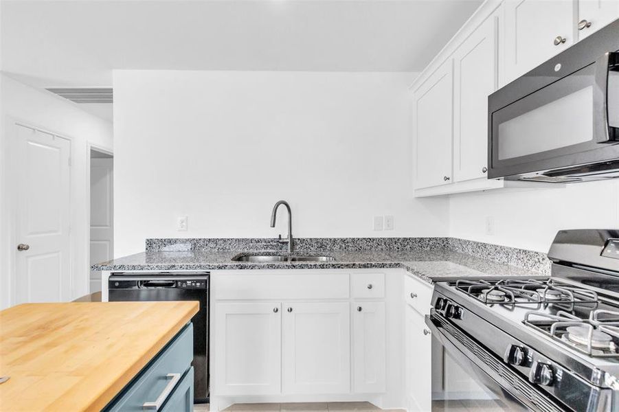 Kitchen with black appliances, white cabinetry, light stone counters, and light tile patterned flooring