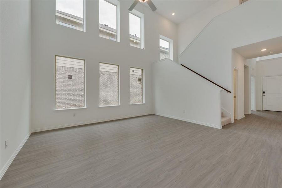 Unfurnished living room featuring ceiling fan, light hardwood / wood-style flooring, and a towering ceiling