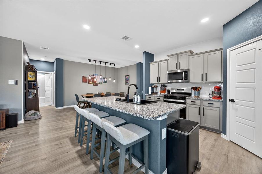 Kitchen with gray cabinetry, a breakfast bar area, stainless steel appliances, a kitchen island with sink, and light wood finished floors