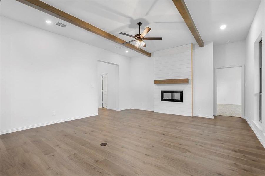 Unfurnished living room featuring beamed ceiling, ceiling fan, light hardwood / wood-style floors, and a fireplace