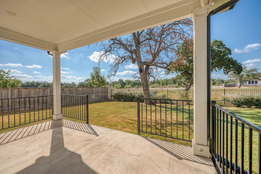 A covered concrete patio overlooks the fenced grassy yard and surrounding mature trees. A covered concrete patio overlooks the fenced grassy yard and surrounding mature trees.