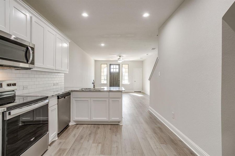 Kitchen featuring stainless steel appliances, white cabinetry, a peninsula, light stone counters, and light wood-type flooring