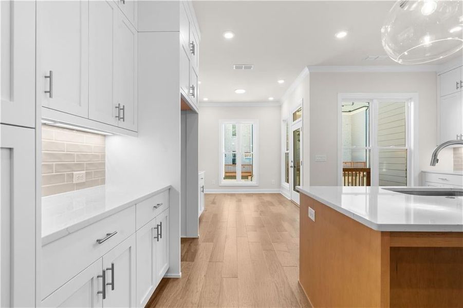 Kitchen with recessed lighting, tasteful backsplash, light stone counters, ornamental molding, and white cabinets