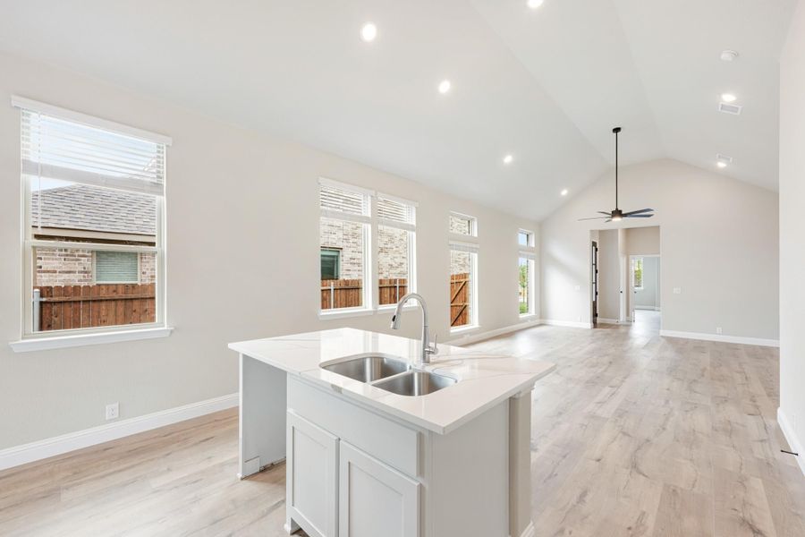 Kitchen island with double sink and white countertop, open to living area with vaulted ceiling and light wood floors