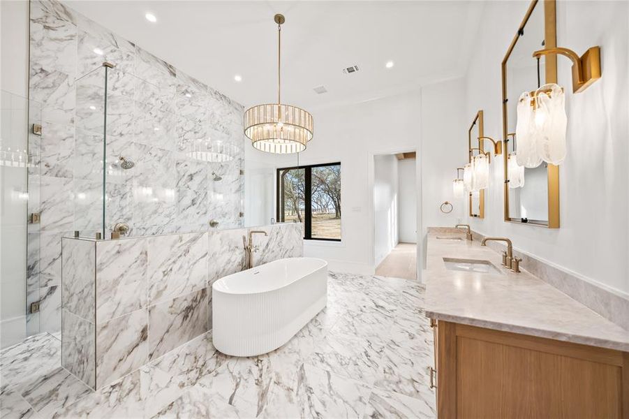 Full bathroom with a marble finish shower, a freestanding bath, light marble finish floors, a chandelier, and double vanity