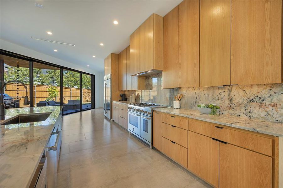 Kitchen featuring light stone counters, premium appliances, tasteful backsplash, and sink