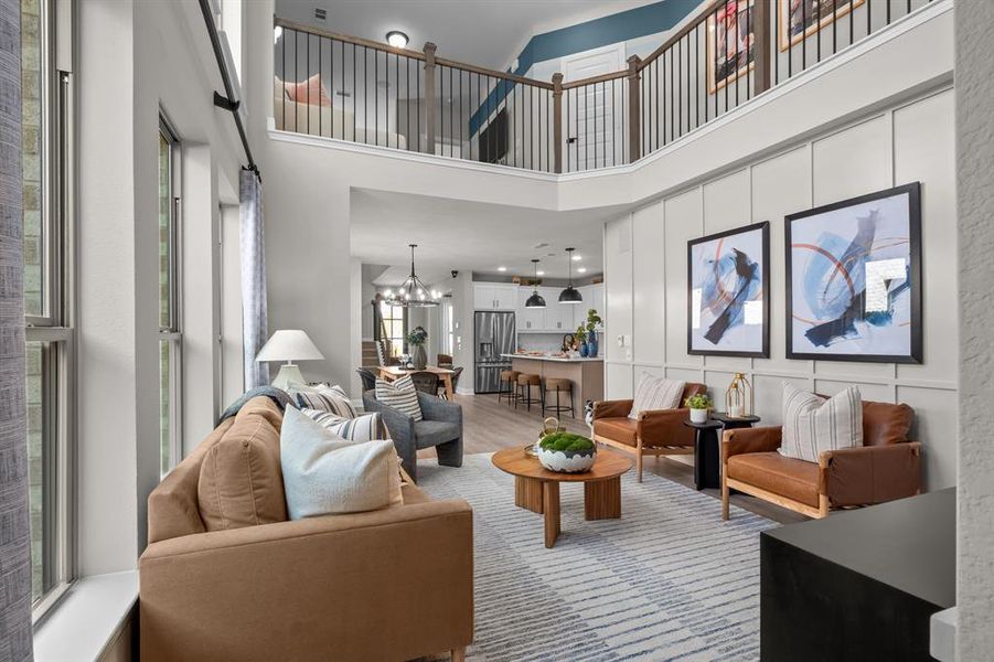 Living room with hanging lights, light wood-style floors, a high ceiling, and a decorative wall
