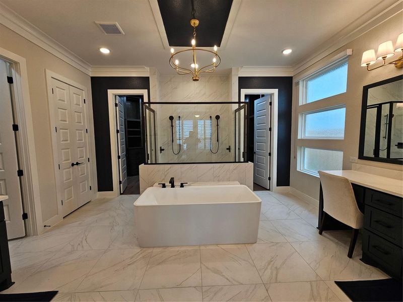 This bathroom features a modern design with a freestanding tub, a glass-enclosed shower, and dual entry doors. It has elegant fixtures, ample natural light from multiple windows, and a sleek vanity with a large mirror, creating a luxurious and spacious feel.