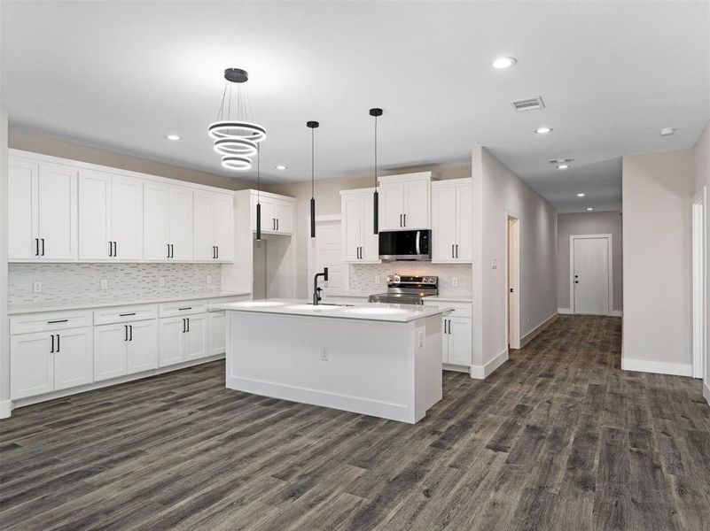 Kitchen featuring appliances with stainless steel finishes, sink, pendant lighting, white cabinets, and an island with sink