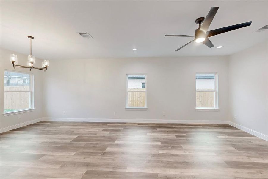 Spare room featuring ceiling fan with notable chandelier and light hardwood / wood-style flooring